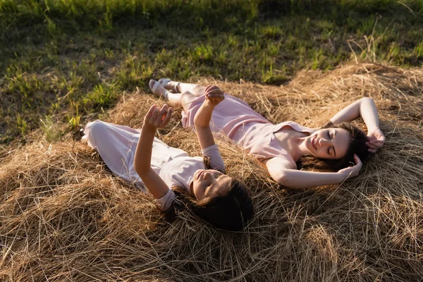 Woman and girl in pink dresses lying on hay in meadow — Foto stock