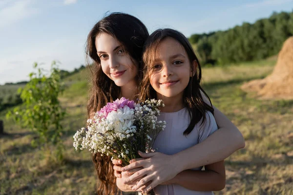 Щаслива жінка і дочка дивляться на камеру біля квіткового букета — стокове фото
