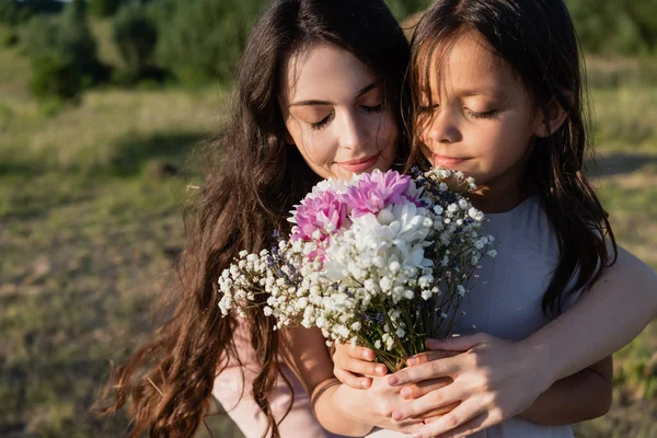 Жінка і дівчина з закритими очима пахнуть букет ароматних квітів — стокове фото