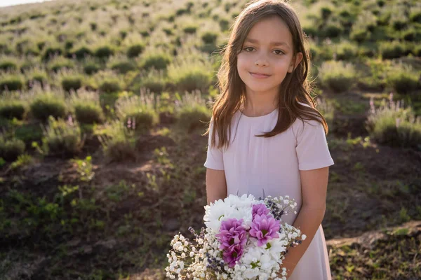 Brunette girl with bouquet looking at camera in green field — Stock Photo