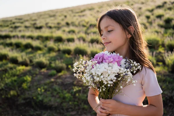 Smiling woman with long hair holding bouquet of flowers in summer field — Stockfoto