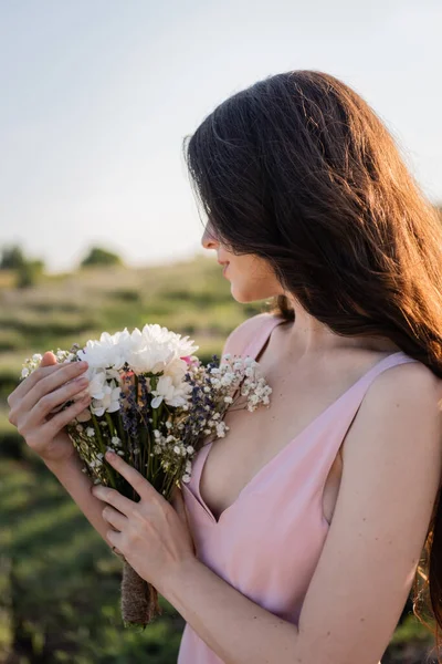 Brunette woman with long hair holding bouquet of summer flowers — Photo de stock