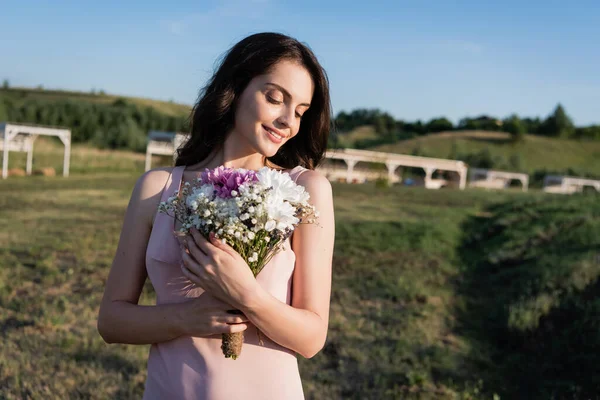 Pretty brunette woman smiling and holding bouquet of summer flowers — Fotografia de Stock
