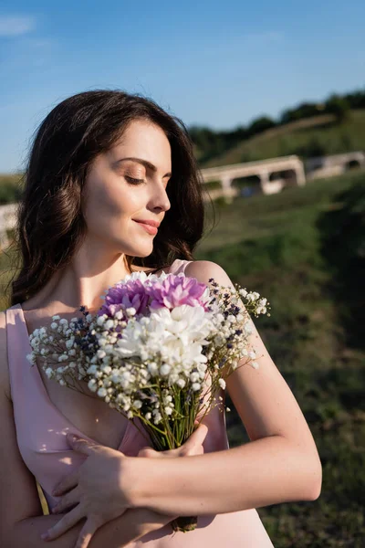 Brunette woman with bouquet of summer flowers smiling outdoors — Stockfoto