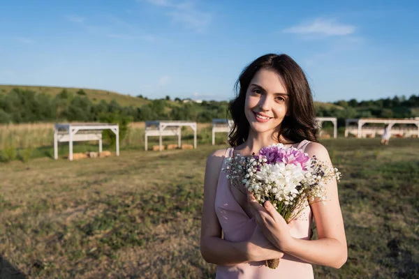 Pleased woman with flowers smiling at camera on farmland — Foto stock
