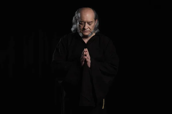 Front view of senior monk with closed eyes and praying hands isolated on black — Stock Photo