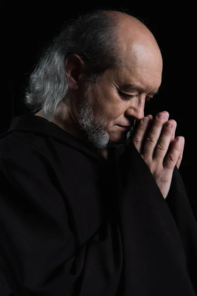 Side view of senior medieval monk with praying hands near face isolated on black — Stock Photo