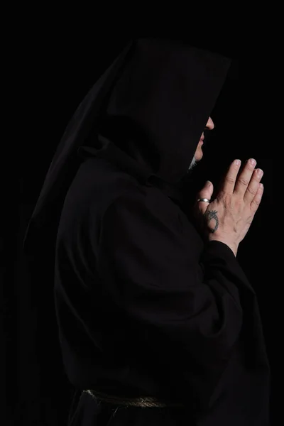 Vue latérale du prêtre tatoué avec le visage obscurci priant isolé sur noir — Photo de stock