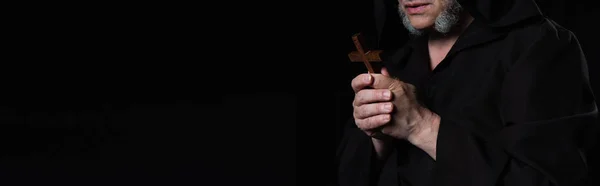Partial view of monk with holy crucifix praying isolated on black, banner — Stock Photo