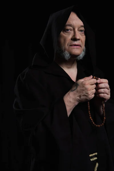 Senior medieval monk with rosary looking at camera isolated on black — Stock Photo