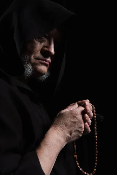 Medieval monk in hood holding rosary isolated on black — Stock Photo