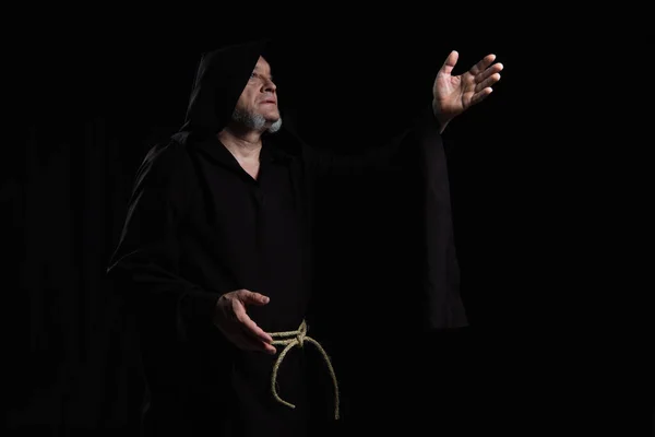 Монах в рясе с капюшоном, указывая рукой, молясь изолированно на черном — стоковое фото
