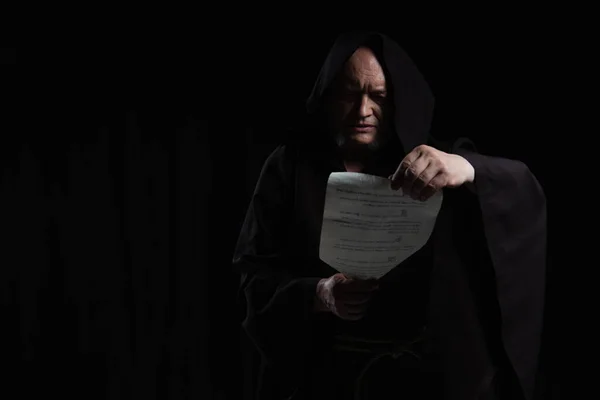 Monk in hooded cassock reading medieval manuscript isolated on black — Stock Photo