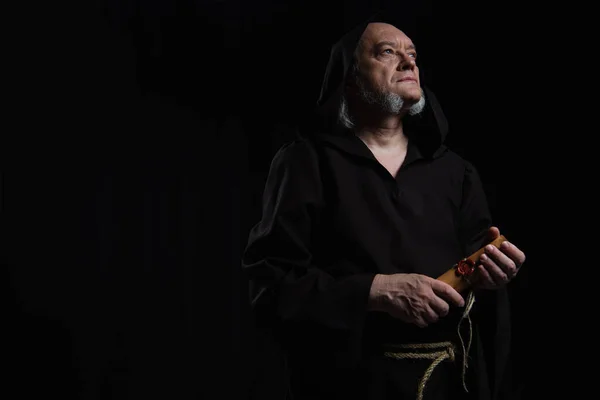 Старший монах з прокатом манускрипт дивиться в сторону ізольовано на чорному — Stock Photo