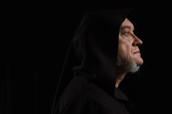 Perfil de monje misterioso en capucha oscura aislado en negro - foto de stock