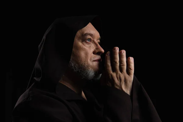 Vista lateral do monge medieval com as mãos de oração perto do rosto isolado no preto — Fotografia de Stock