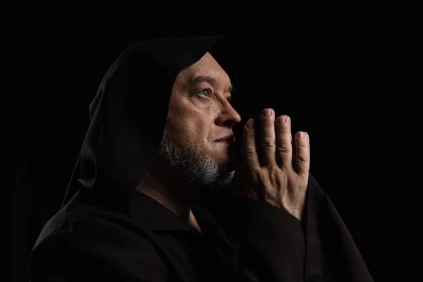 Side view of medieval monk with praying hands near face isolated on black — Stock Photo