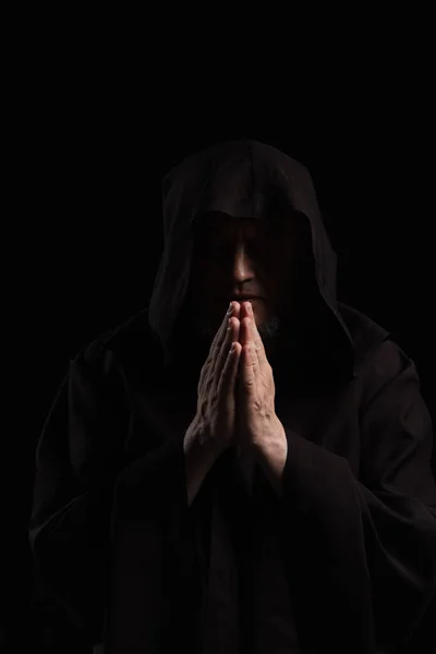 Front view of monk in dark hooded cassock praying isolated on black — Stock Photo