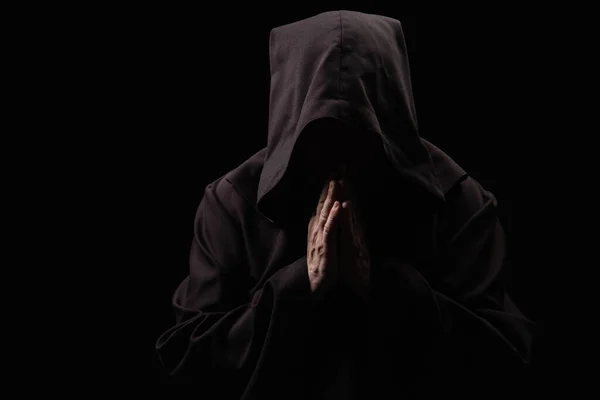 Mittelalterlicher Mönch mit Gesicht unter dunkler Kapuze, der isoliert auf schwarz betet — Stockfoto