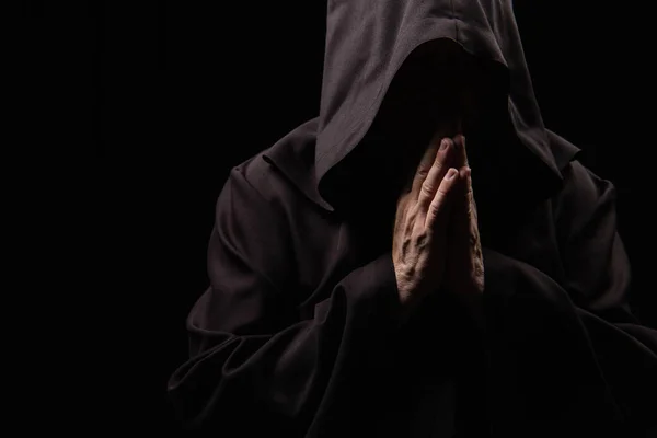 Anonymous medieval monk in hood praying isolated on black — Stock Photo