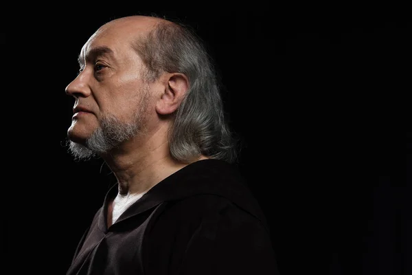 Portrait de profil de moine sénior aux cheveux gris et à la barbe regardant loin isolé sur noir — Photo de stock