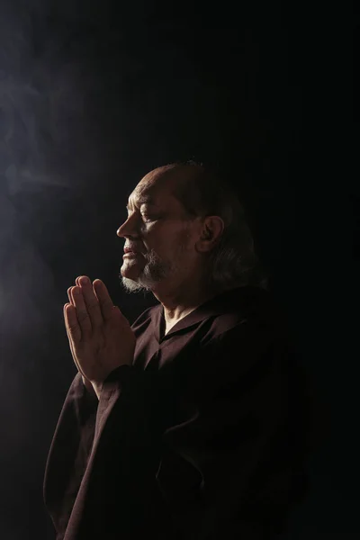 Medieval priest with closed eyes praying at night on black background — Stock Photo