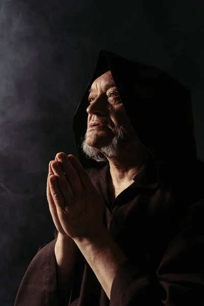 Senior priest with praying hands looking away on black background — Stock Photo