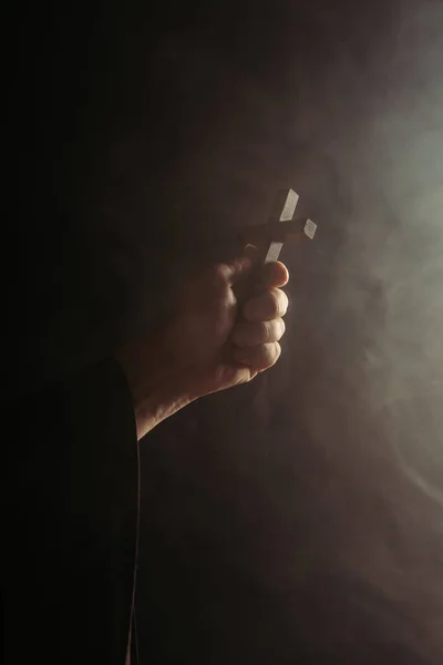 Partial view of monk with holy cross in hand on black background with smoke — Stock Photo