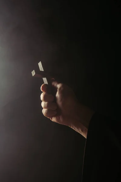 Partial view of priest holding holy crucifix on black background — Stock Photo