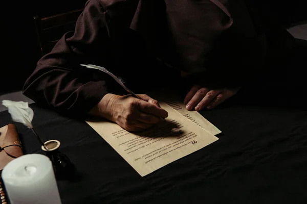 Medieval monk with bowed head writing manuscript on parchment isolated on black — Stock Photo