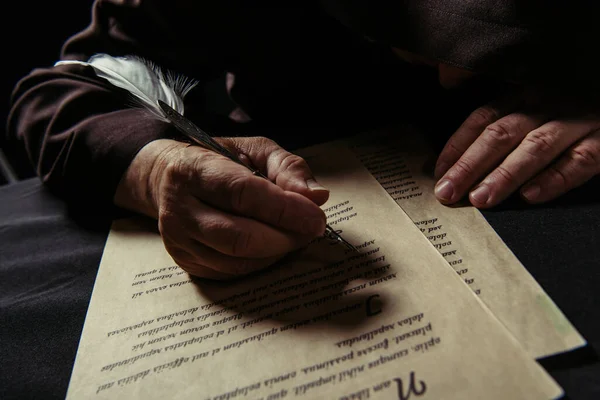 Medieval monk with bowed head writing manuscript with quill pen on parchment isolated on black — Stock Photo