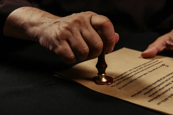 Cropped view of monk stamping chronicle with wax seal isolated on black — Stock Photo