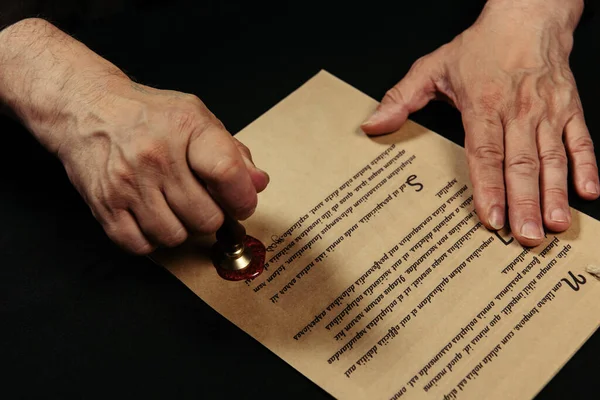 Top view of cropped monk stamping manuscript with wax seal on black table — Stock Photo