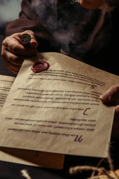 Partial view of monk holding parchment with manuscript and wax seal on dark background — Stock Photo