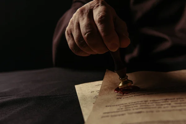 Cropped view of abbot holding wax seal near parchment with chronicle isolated on black — Stock Photo