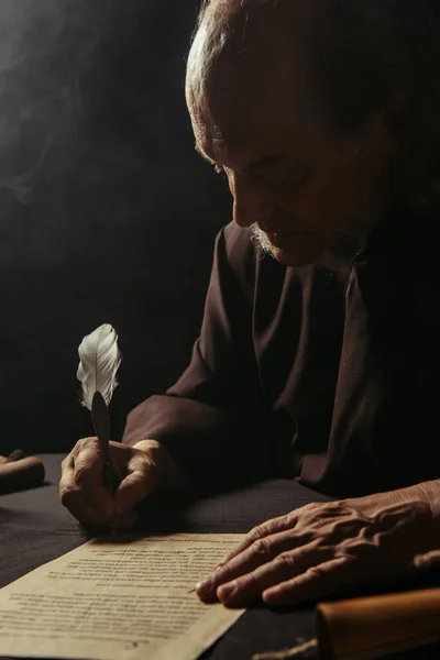 Cronista medievale che scrive manoscritto antico con penna a penna di notte su sfondo nero — Foto stock