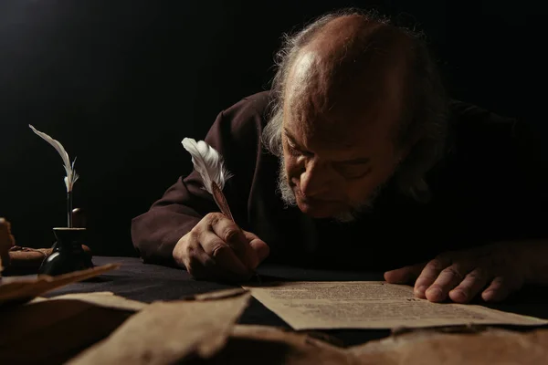 Senior abbot writing manuscript on parchment isolated on black — Stock Photo