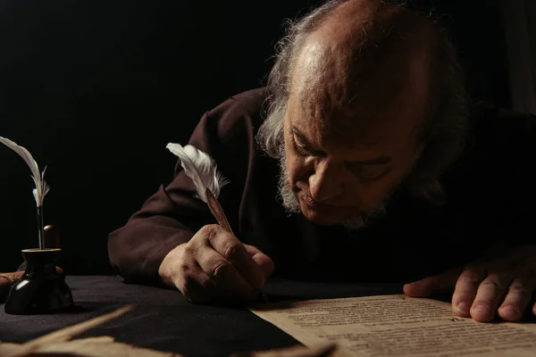 Medieval chronicler writing manuscript with feather pen isolated on black — Stock Photo