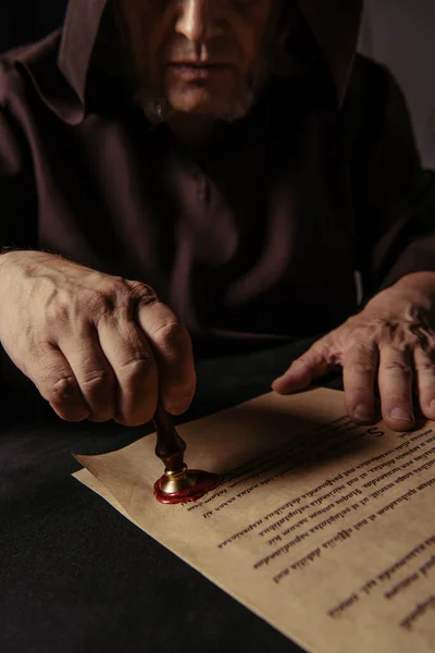 Cropped view of priest putting wax seal on ancient chronicle isolated on black — Stock Photo