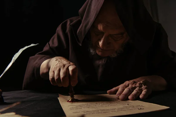 Medieval monk stamping manuscript with wax seal at night isolated on black — Stock Photo