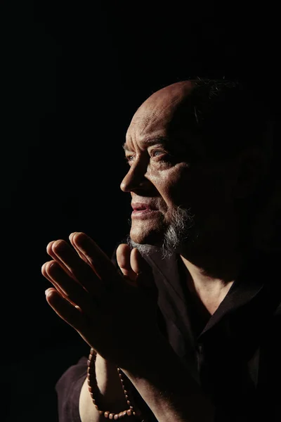 Senior bearded priest looking away while praying isolated on black — Stock Photo