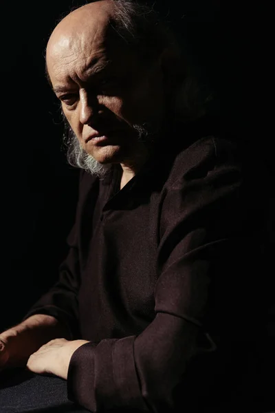 Strict and thoughtful priest looking at camera isolated on black — Stock Photo