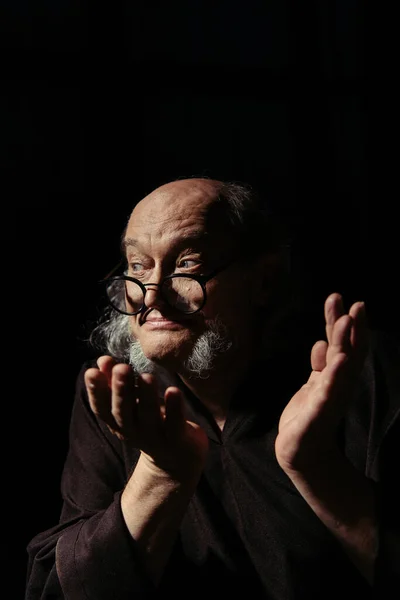 Thoughtful medieval philosopher in eyeglasses showing shrug gesture isolated on black — Stock Photo