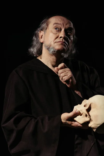 Filosofo religioso medievale con teschio alzando lo sguardo mentre pensa isolato sul nero — Foto stock