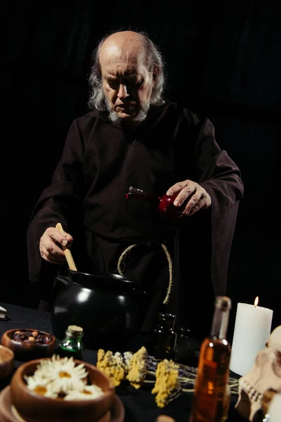 Senior Alchemist Flüssigkeit hinzufügen, während Kochen Trank in der Nacht isoliert auf schwarz — Stockfoto