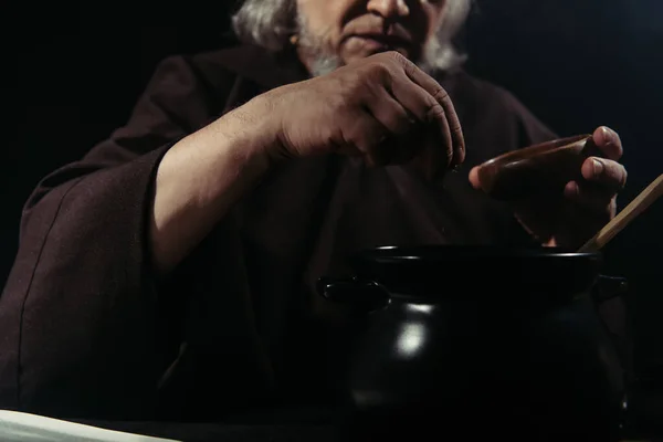Cropped view of blurred alchemist adding ingredient into pot isolated on black — Stock Photo