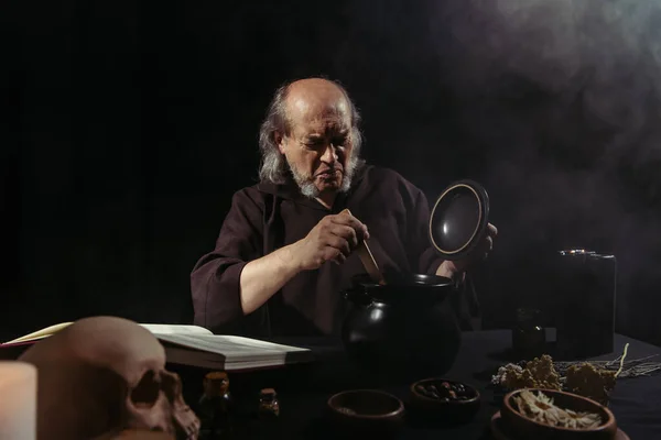 Médiévale froncement de sourcils alchimiques près de la marmite à vapeur sur fond noir — Photo de stock