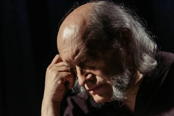 Senior religious philosopher holding hand near bowed head while thinking isolated on black — Stock Photo