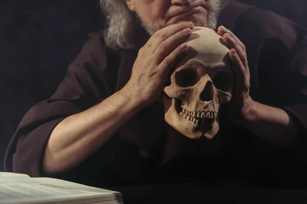 Cropped view of philosopher holding skull near blurred bible isolated on black — Stock Photo