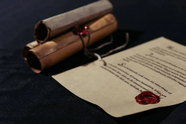 Old manuscript stamped with wax seal near rolled parchments on black background — Stock Photo